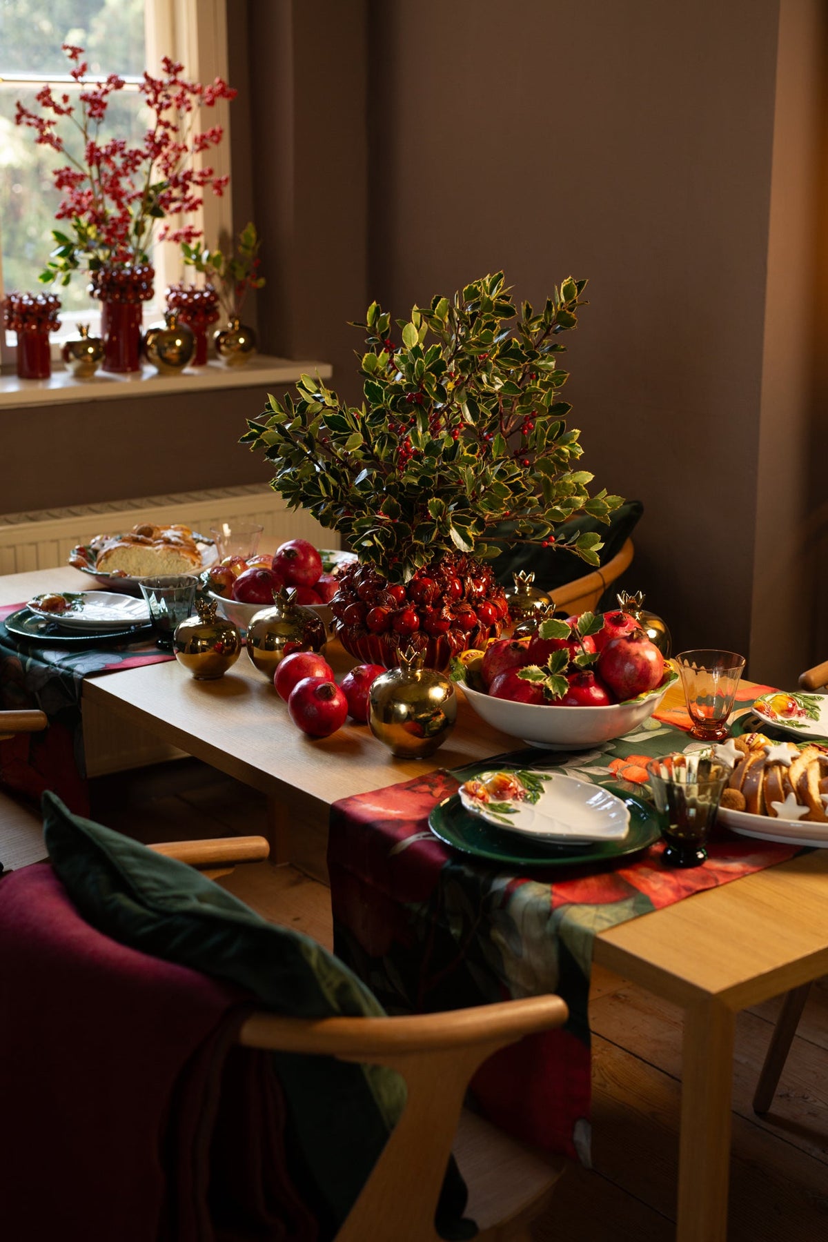 Festively set table with red apples, pomegranates, gold baubles and green branches.