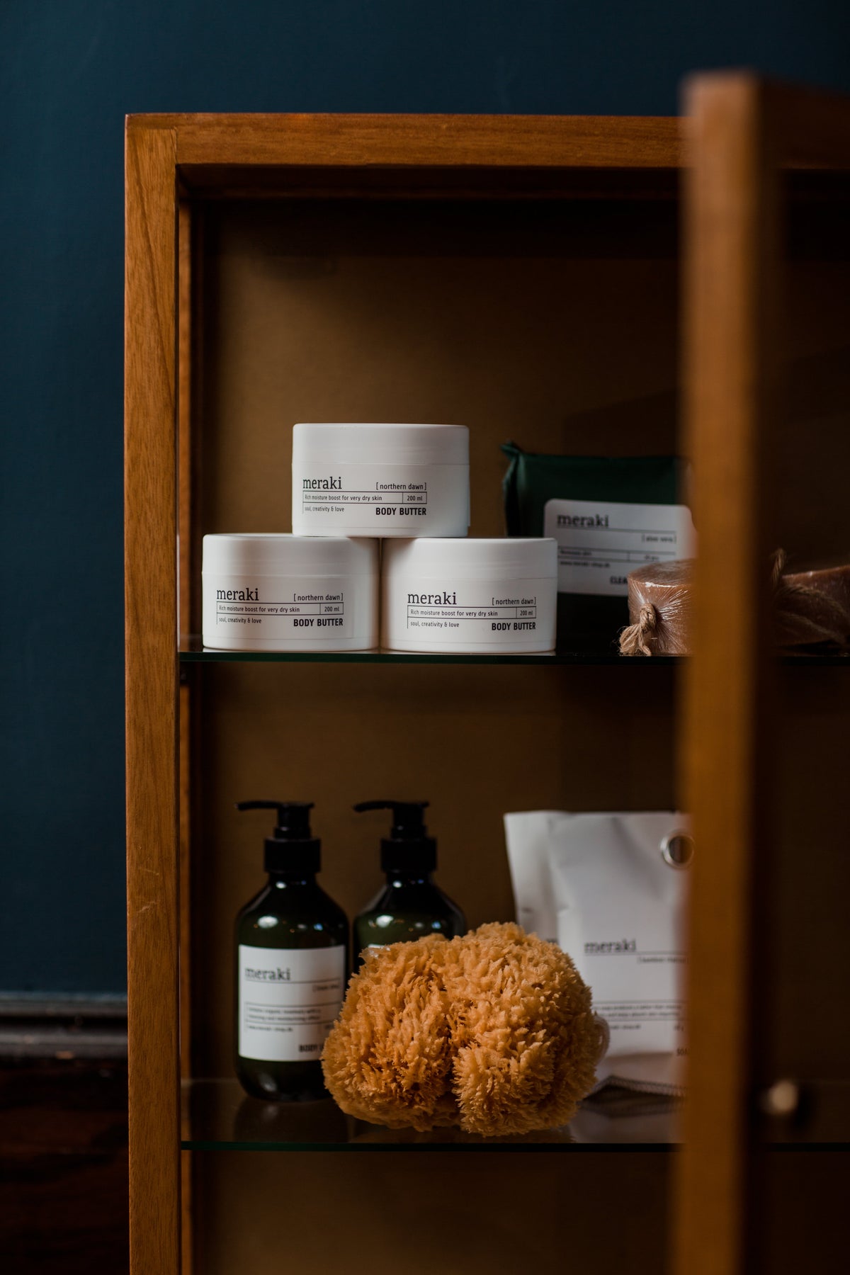 Premium body care products featuring body butter, soaps and natural bath sponges, beautifully arranged on warm wooden shelves.