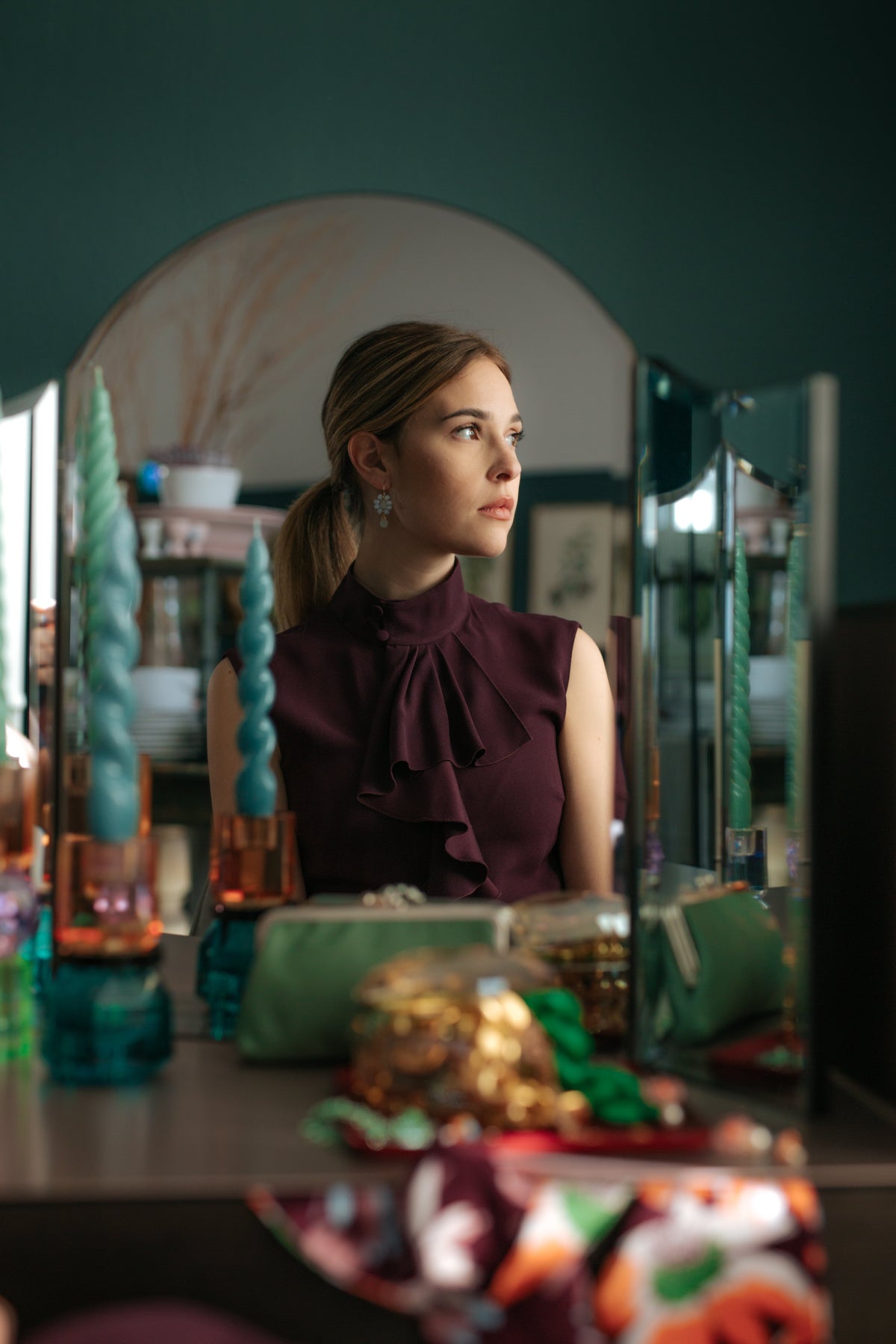Woman in a burgundy top in front of a mirror with decorative candles.