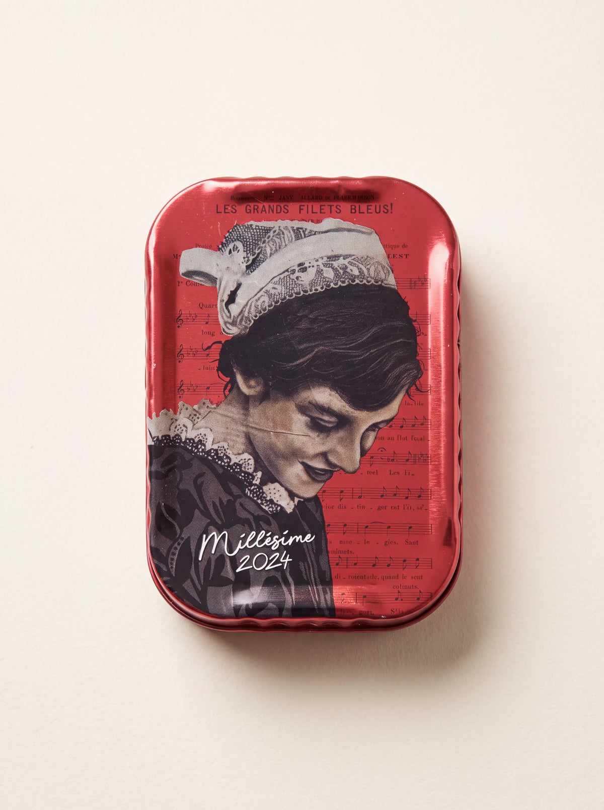 Red vintage sardine tin featuring an illustrated Breton woman over sheet music and the text Millésime 2024