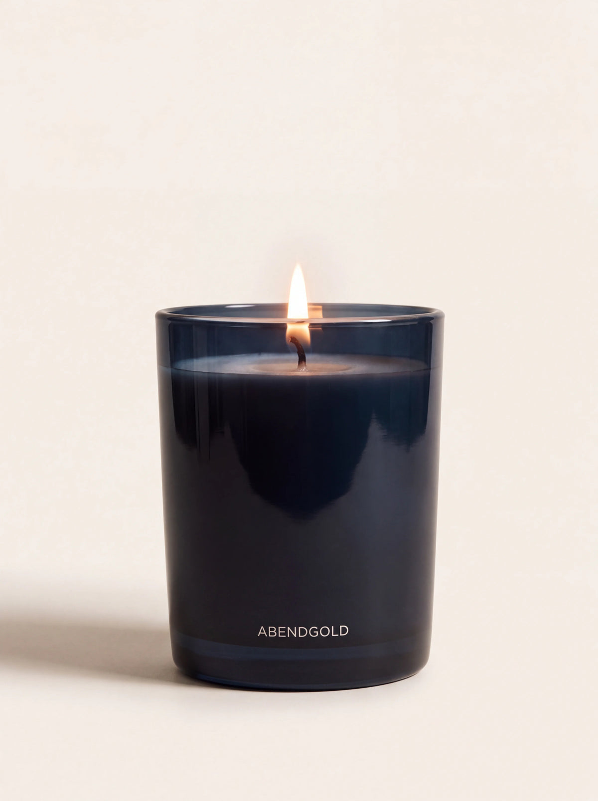 Lit scented candle in a dark blue glass jar with ABENDGOLD printed near the base