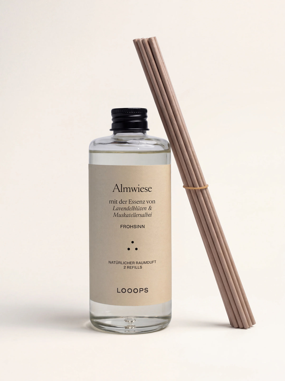 Reed diffuser refill in a clear glass bottle with black cap and paper label, beside a bundle of reed sticks