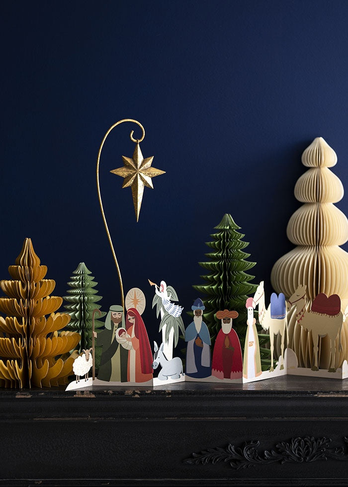 Paper honeycomb tree displayed on a dark shelf beside an illustrated nativity scene