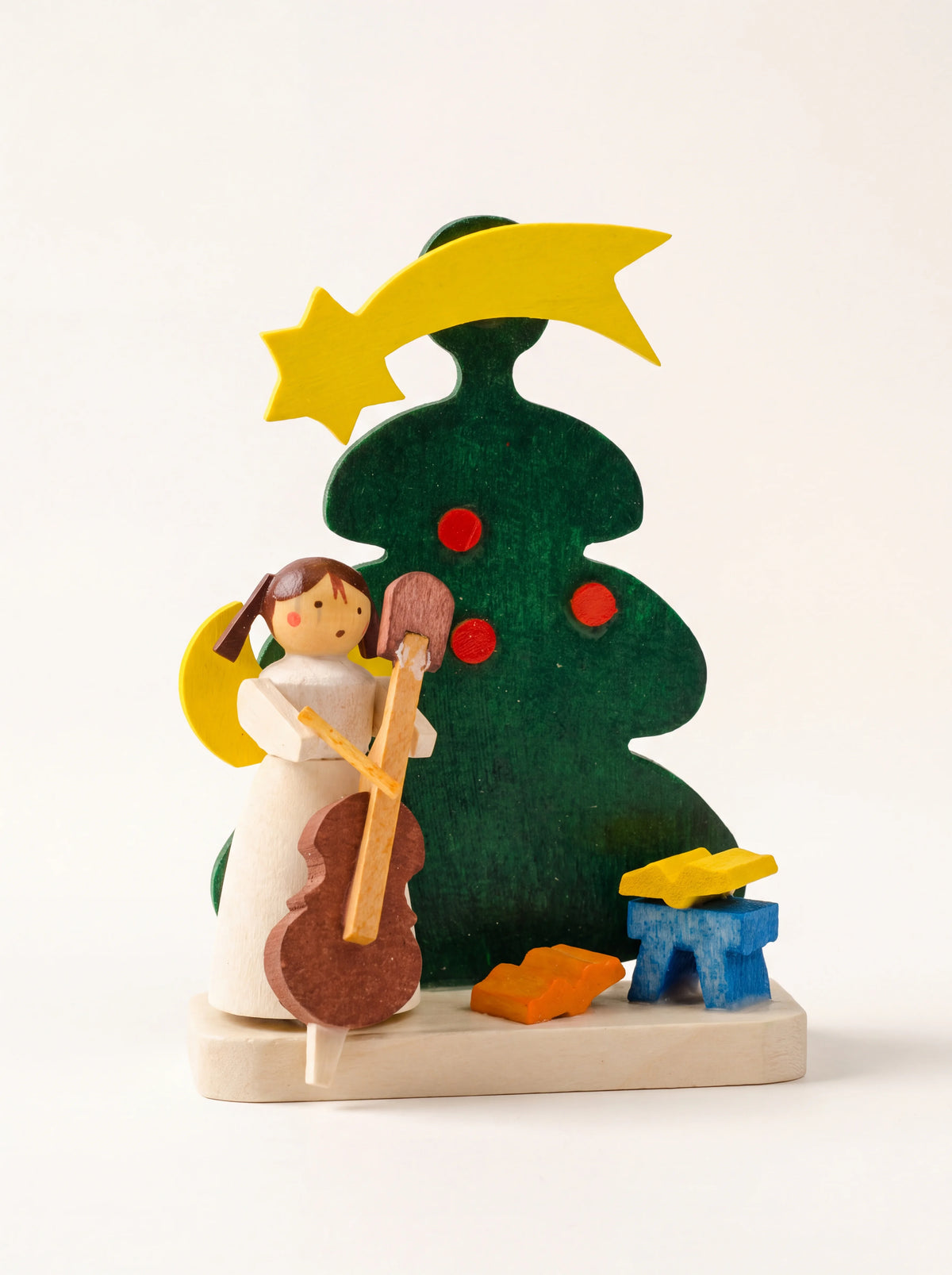 Wooden angel ornament playing a cello beside a green Christmas tree with a shooting star