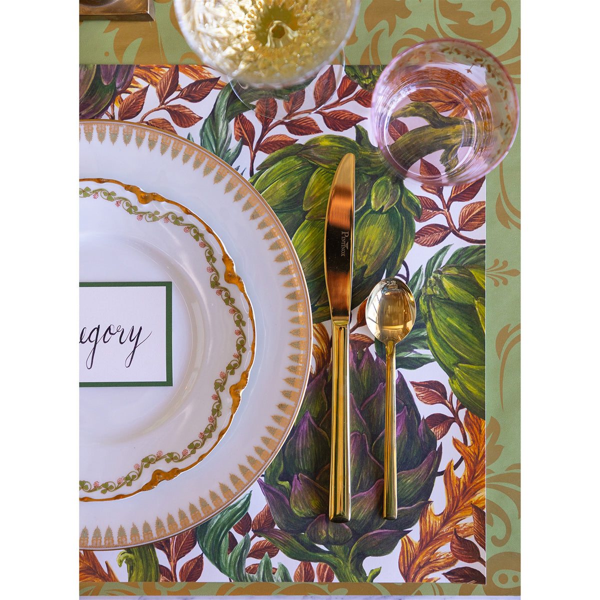 Close-up of the artichoke paper placemat under a gold-rimmed plate and gold cutlery
