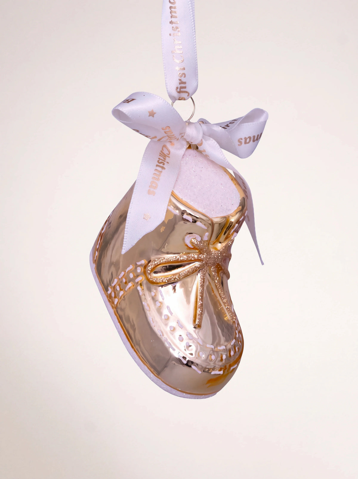 Shiny gold glass baby shoe ornament with glitter laces and white ribbon reading Baby's first Christmas