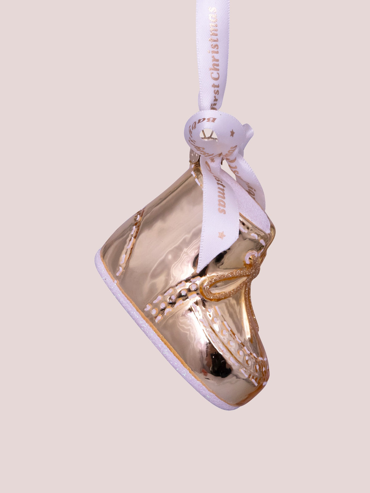 Side view of the gold glass baby shoe ornament showing painted white stitching along the upper