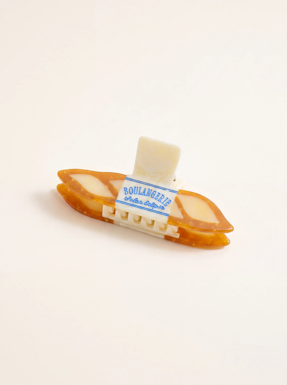 Baguette claw hair clip in amber and cream cellulose acetate with blue text reading BOULANGERIE Solar Eclipse