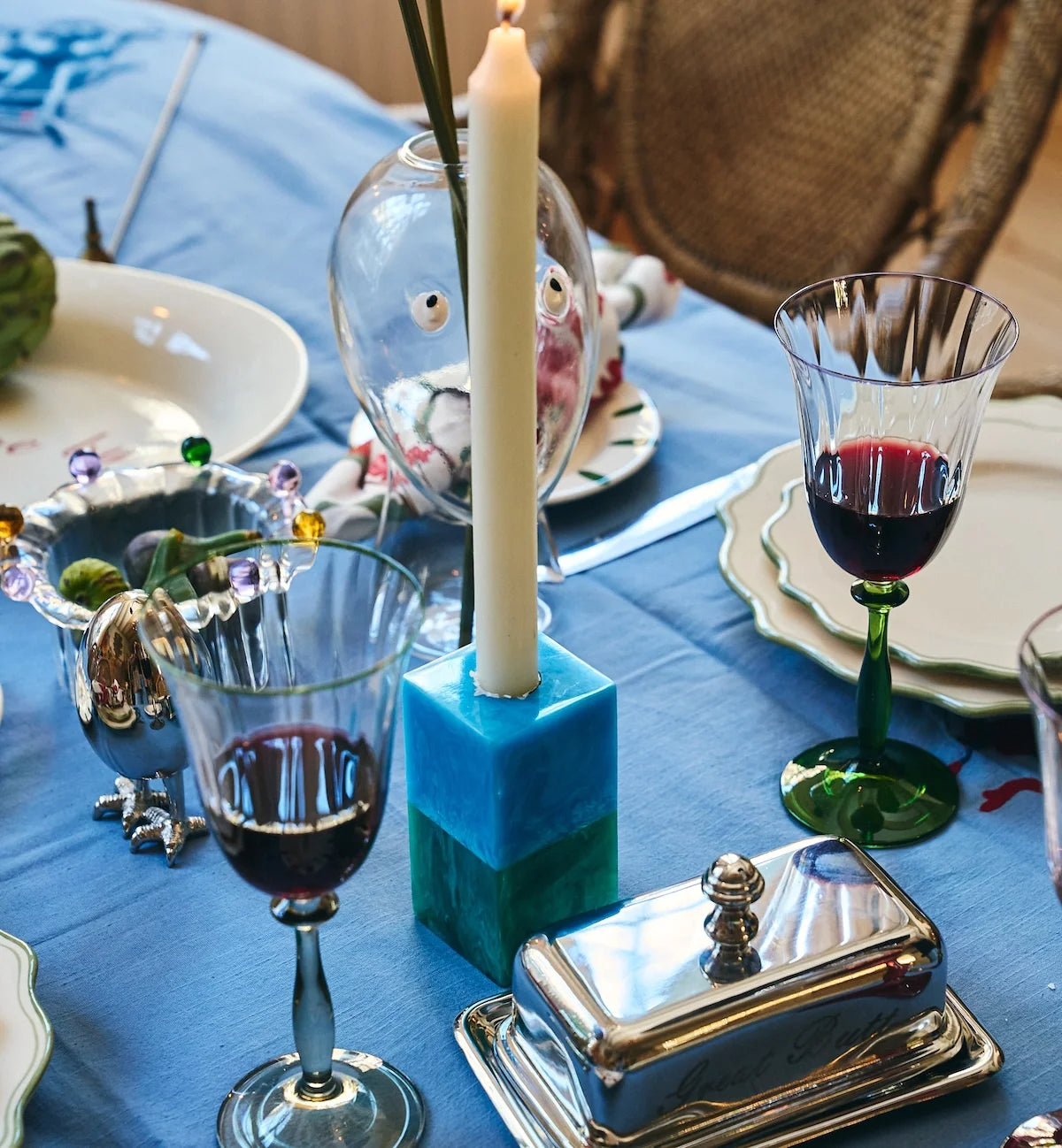 Two-tone resin candle holder holding a lit white taper candle on a laid dining table