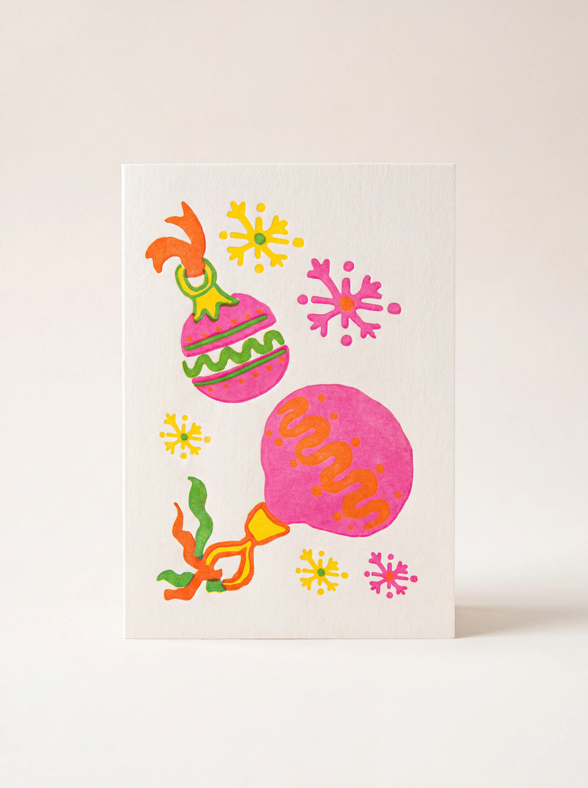 Paper greeting card illustrated with bright pink baubles, ribbons and colourful snowflakes