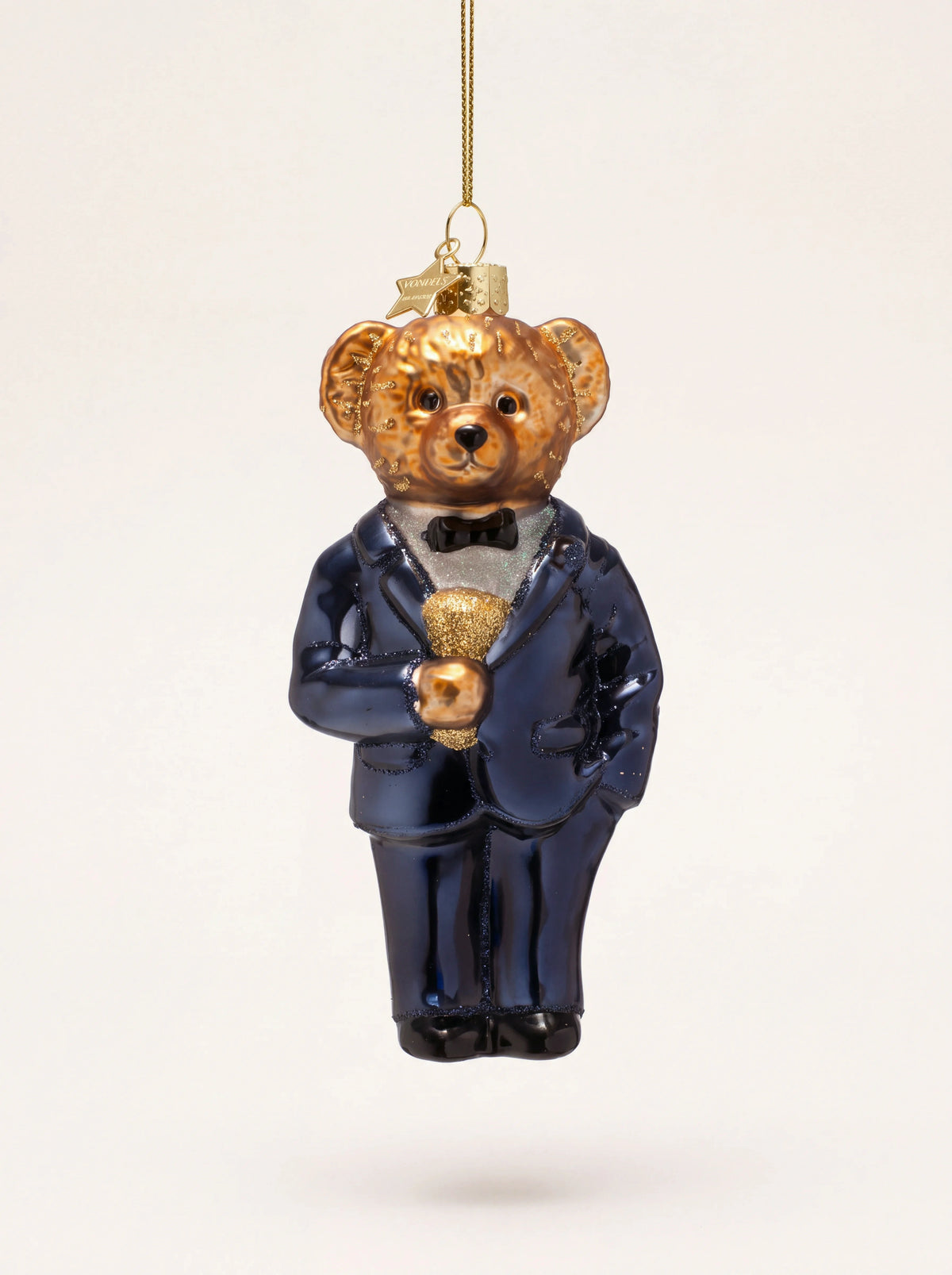 Glass bear ornament wearing a dark blue suit and black bow tie, suspended by a gold hanging string