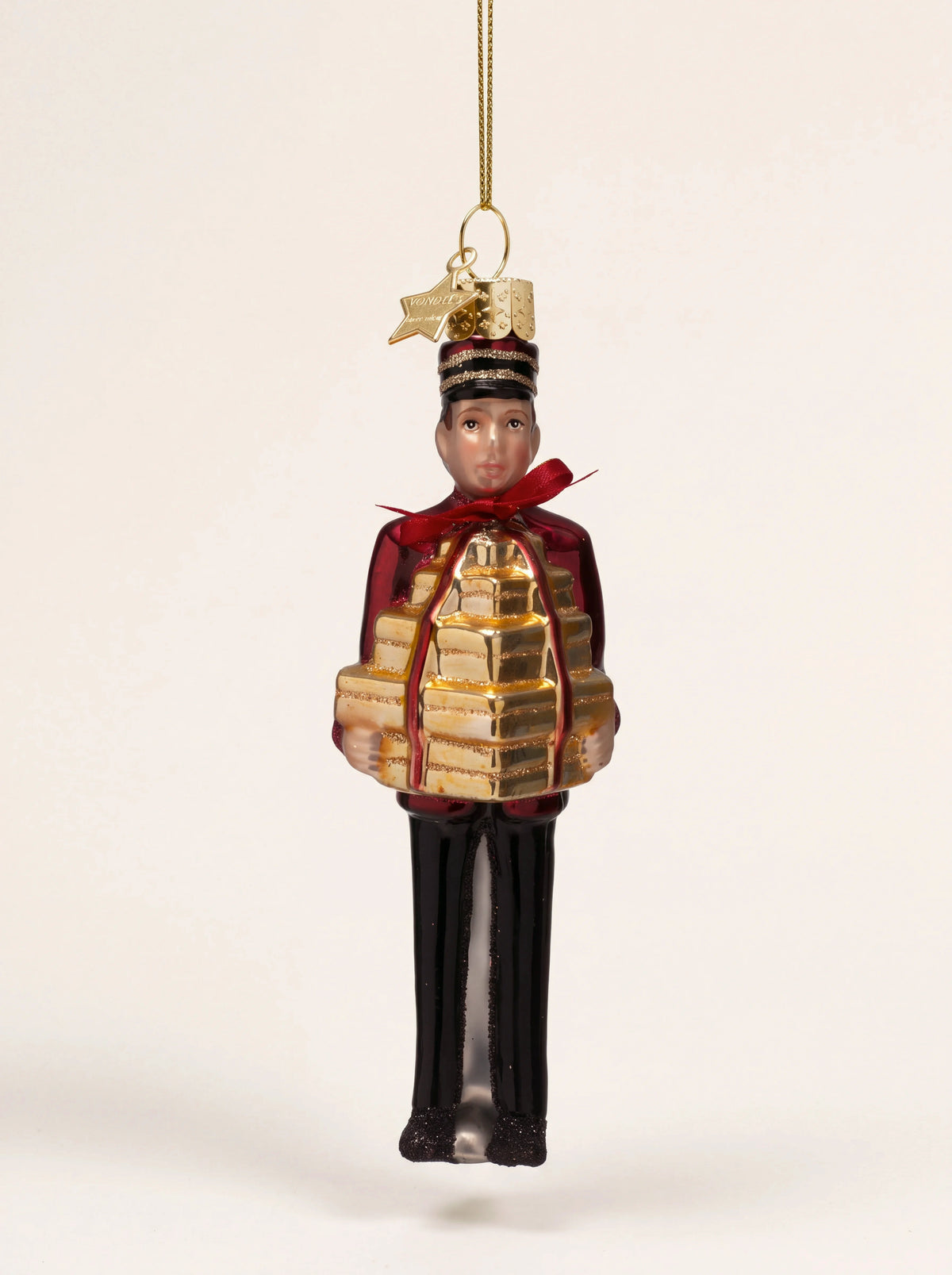 Glass bellboy Christmas ornament in a red jacket holding a stack of gold parcels