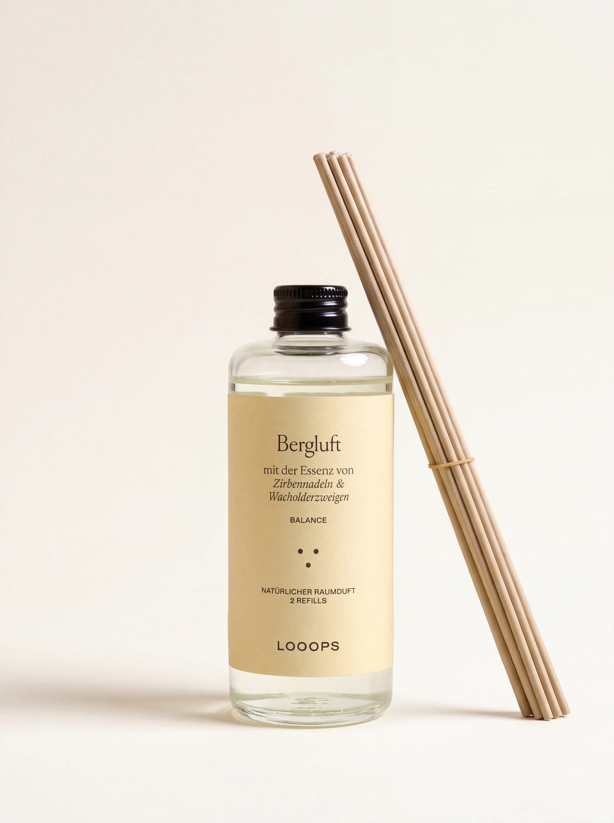 Clear glass bottle of Bergluft reed diffuser refill with black screw cap and bundle of diffuser reeds