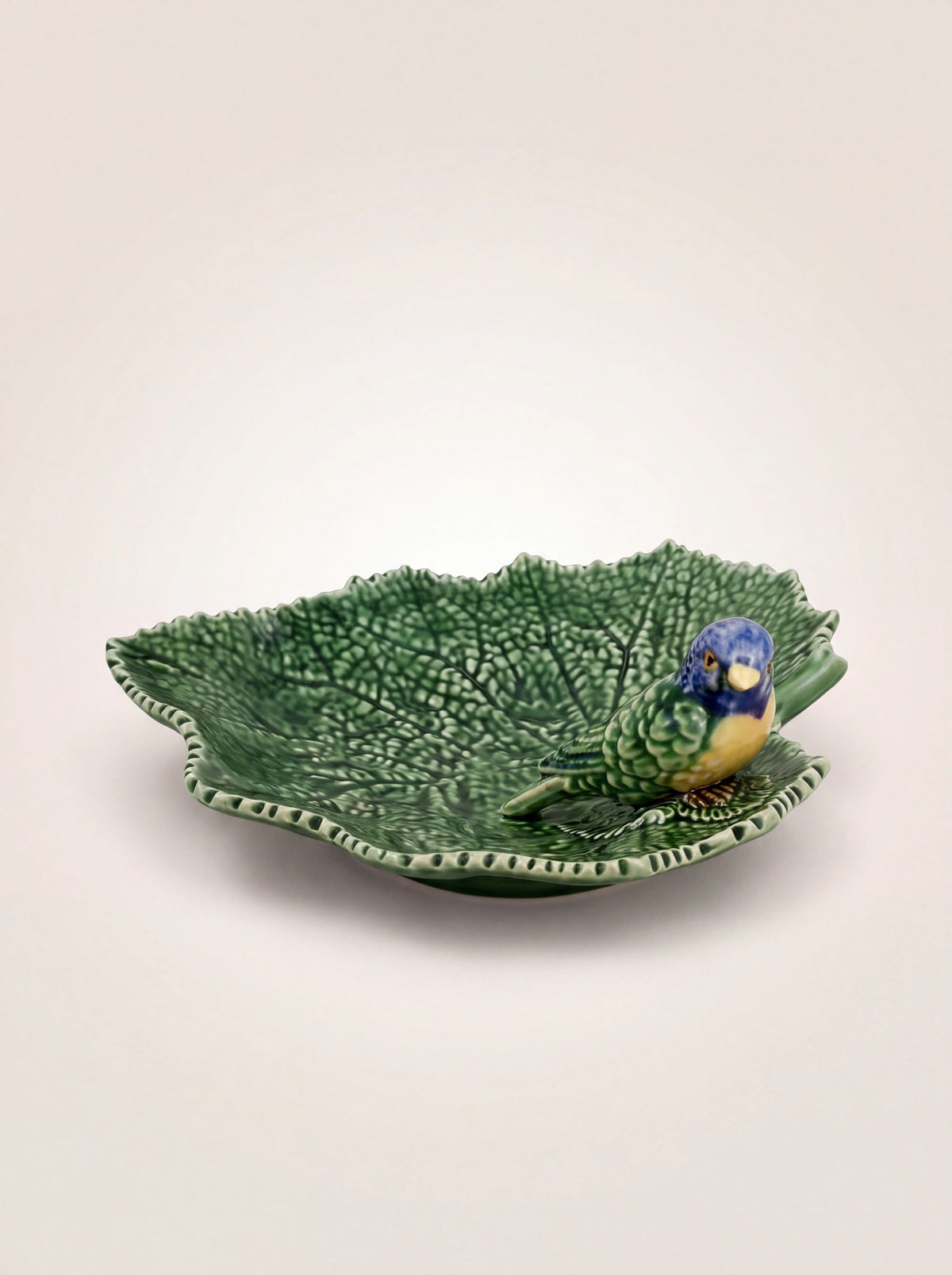 Green glazed earthenware leaf dish with embossed veins and a sculpted blue bird perched inside