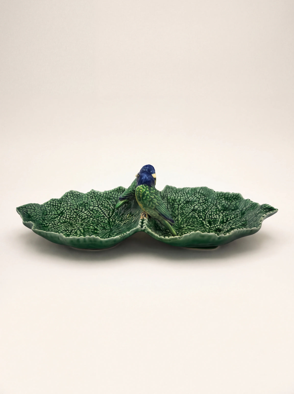 Glazed earthenware dish shaped like two textured green leaves with two birds perched in the centre