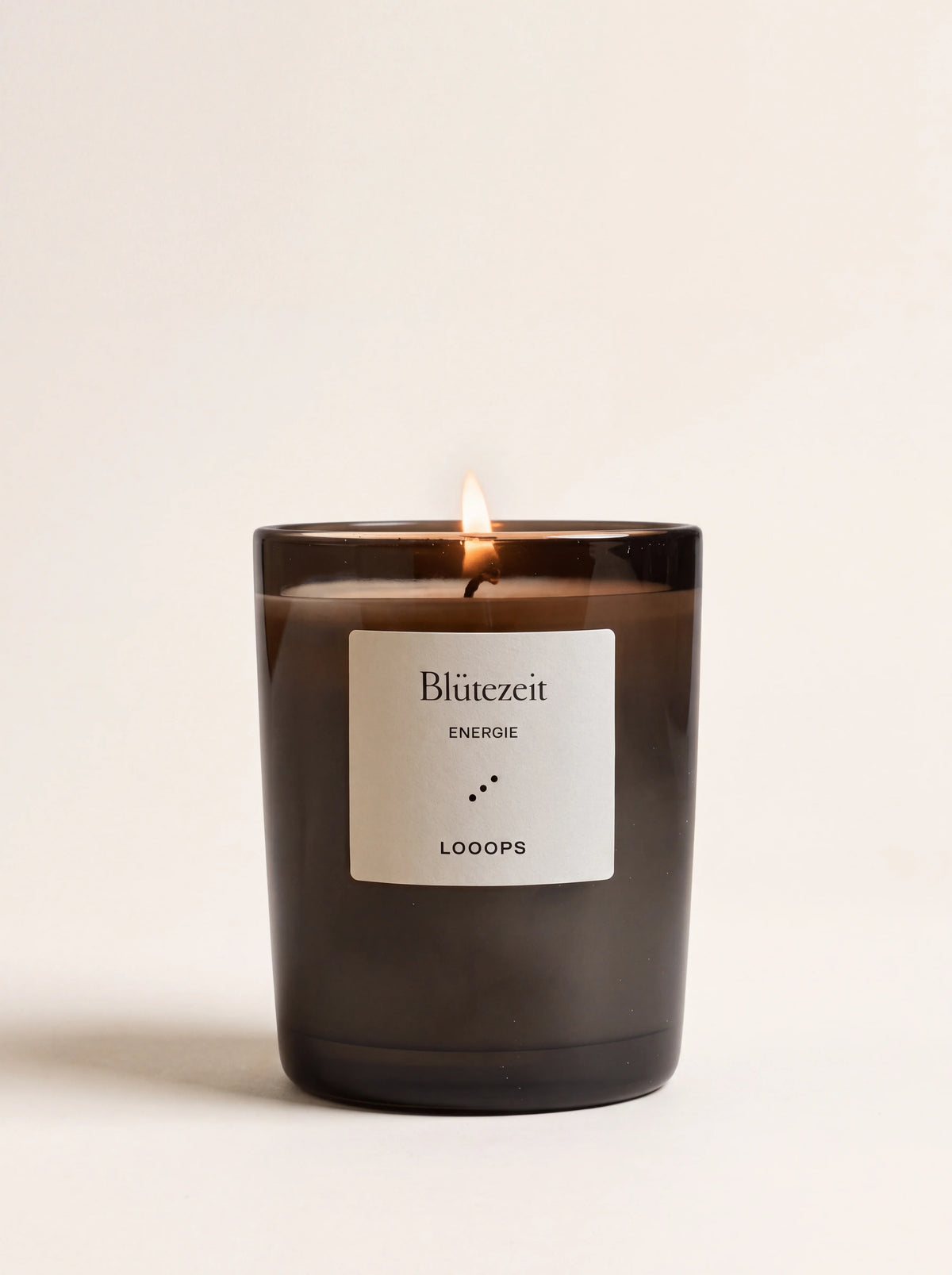 Lit plant wax scented candle in a dark glass jar with a white label reading Blütezeit Energie