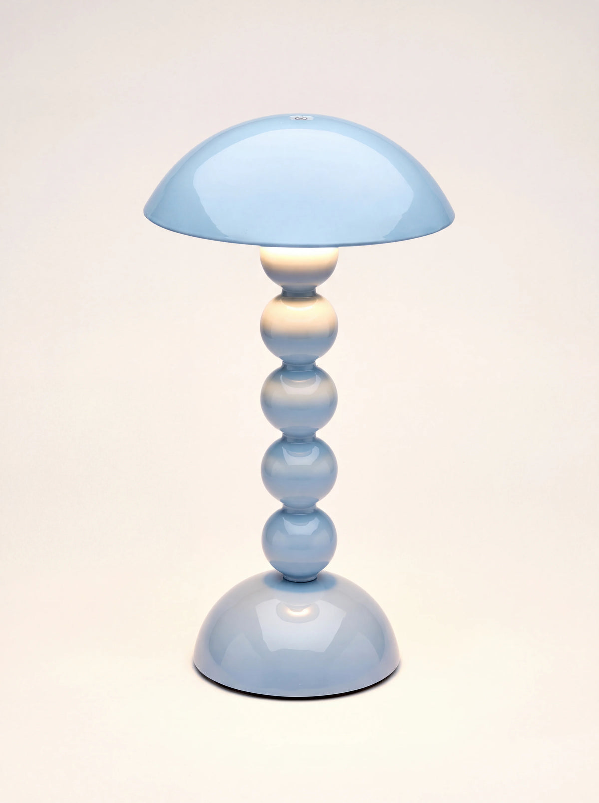 Pale denim bobbin LED lamp turned on, casting a warm glow downwards along the stem