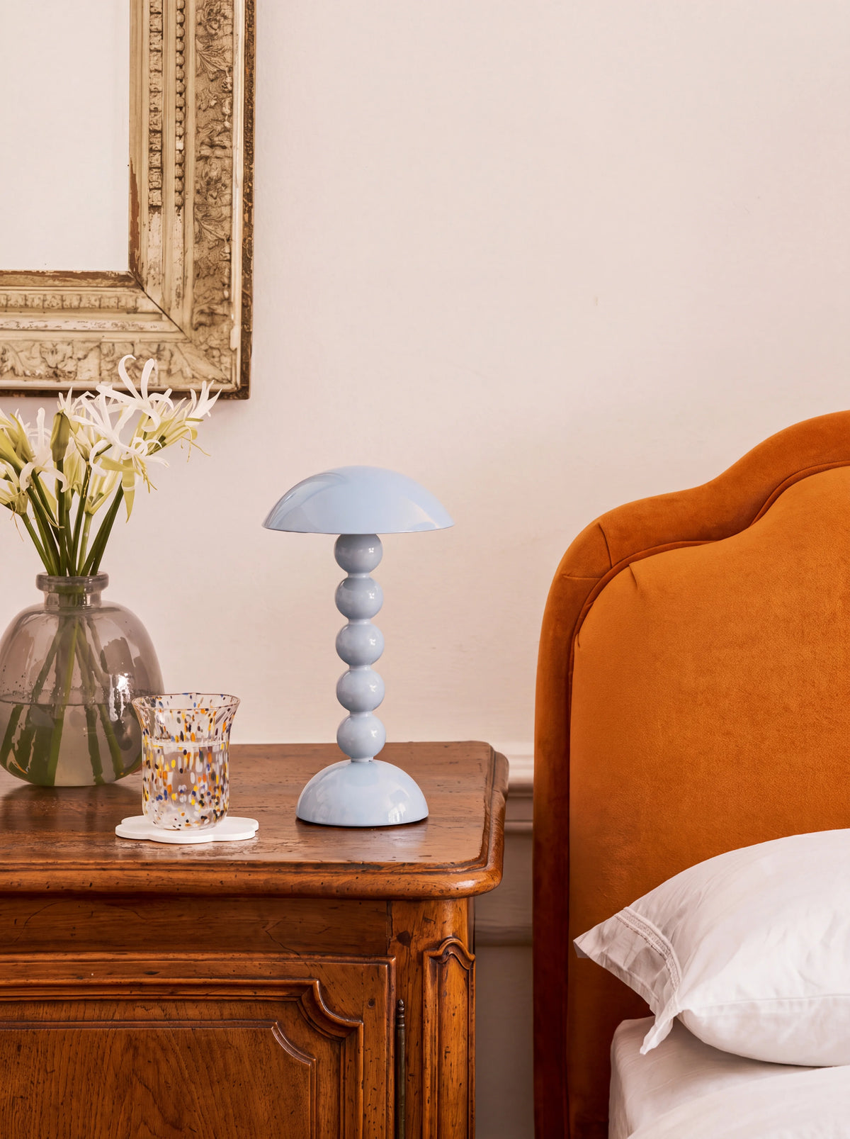Pale denim bobbin LED lamp on a wooden bedside table beside a vase of flowers