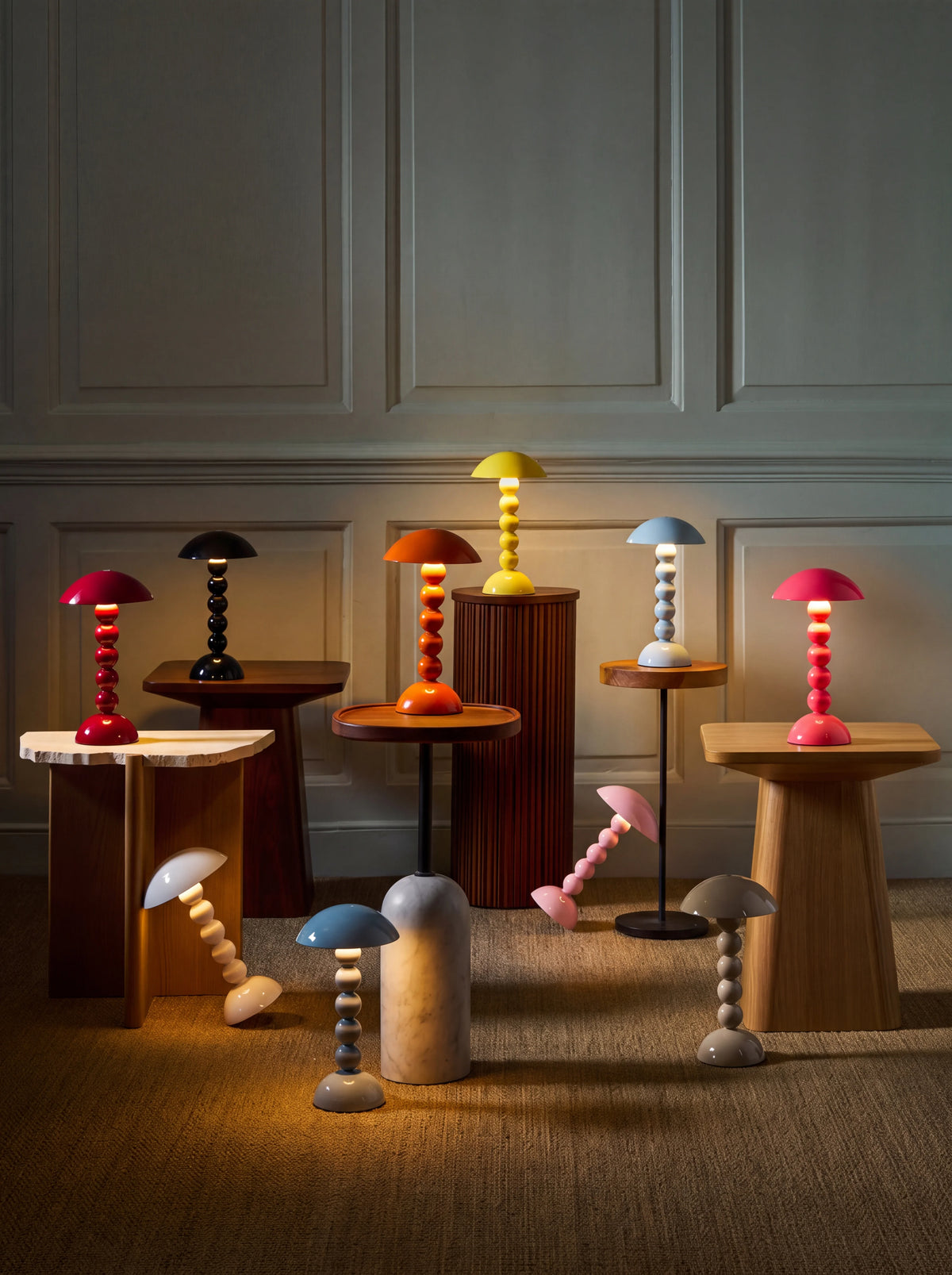 Bobbin table lamps lit up in various colours, displayed on wooden side tables and the floor