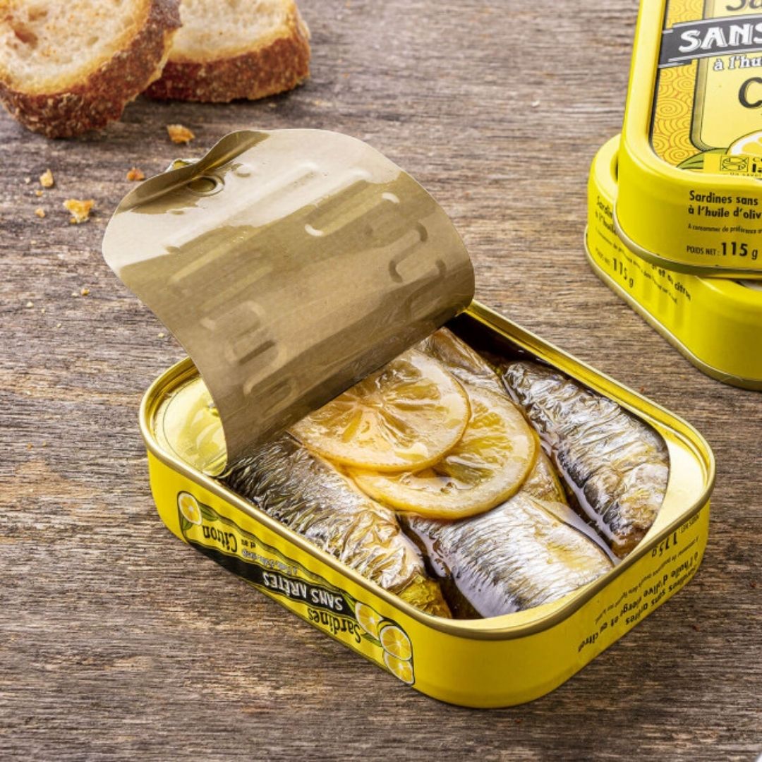 Opened tin revealing boneless sardines in olive oil topped with sliced lemon