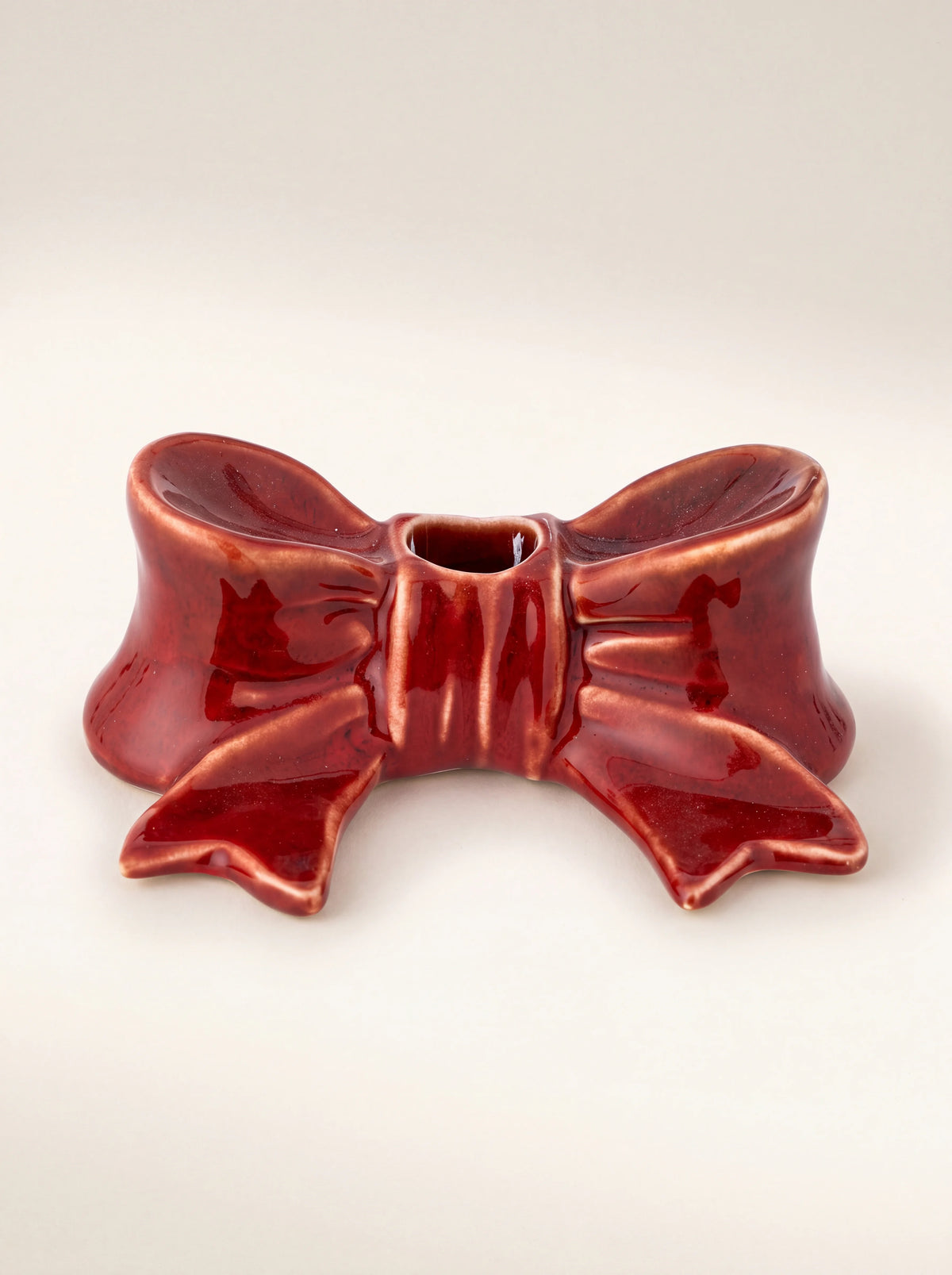 Bow-shaped stoneware candle holder in glossy red glaze with a central candle opening