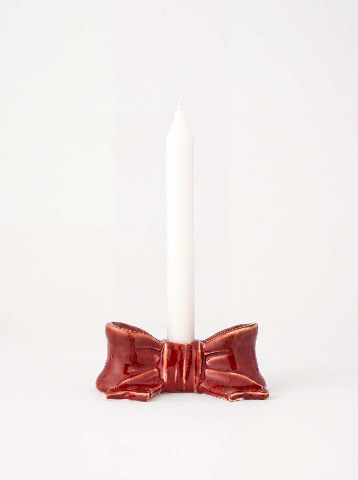 Red ceramic bow candle holder shown holding a tall white taper candle