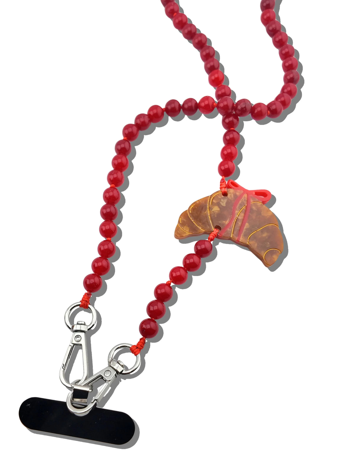 Close-up of the hand-painted croissant charm with red bow detail, knotted cord and clasp