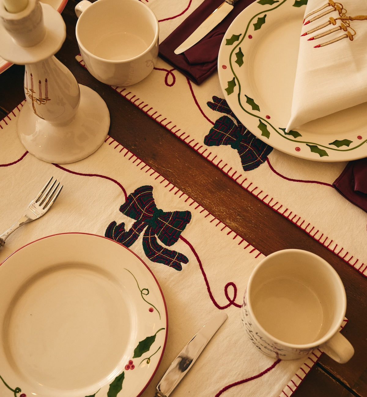 Cotton placemats laid on a wooden dining table, set with ceramic plates, cutlery, mugs, and a candlestick