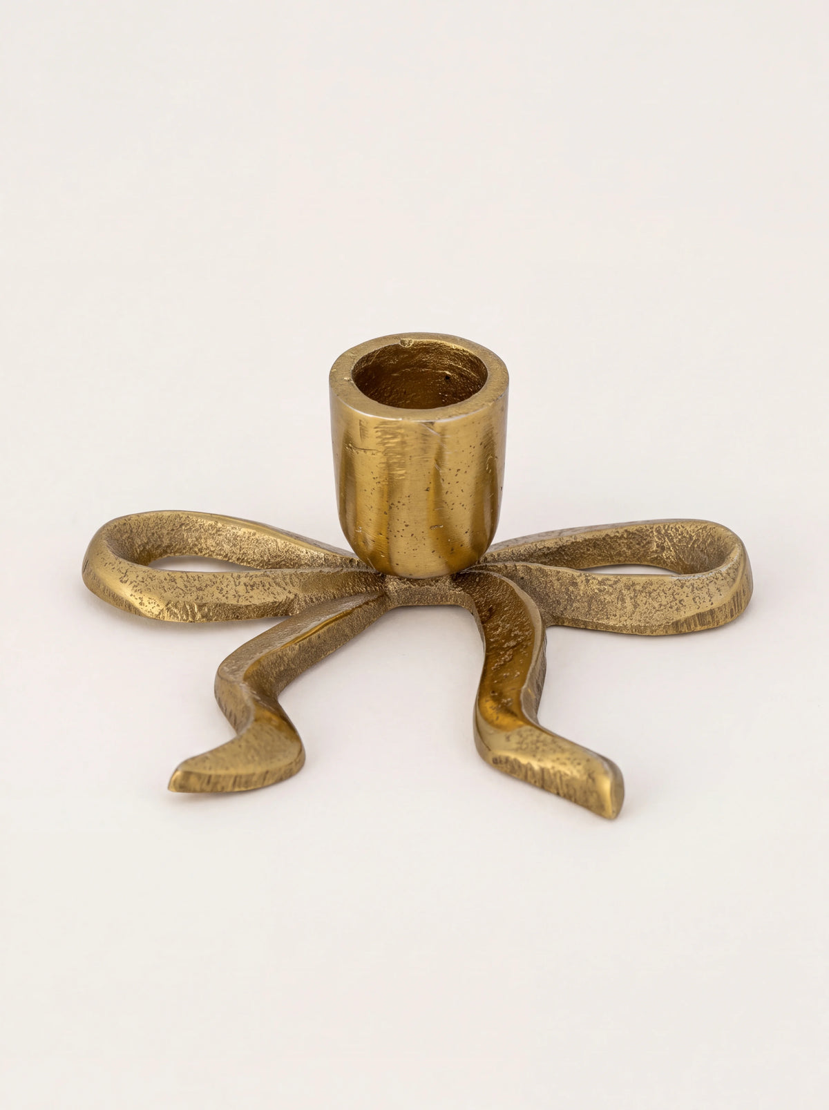 Bow-shaped aluminium candle holder with a textured gold finish and central candle cup
