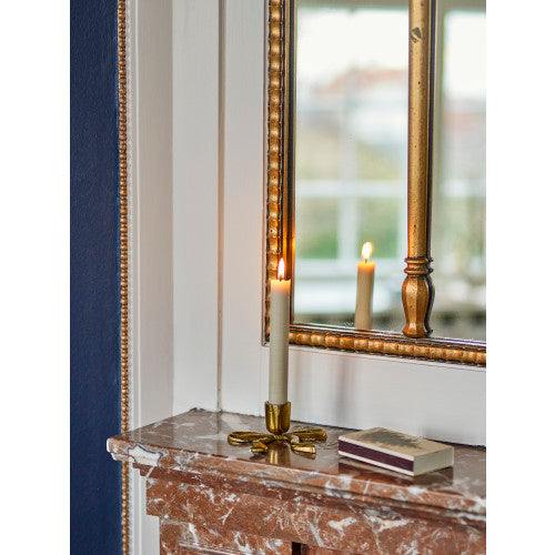 Bow-shaped candle holder in use with a lit taper candle on a marble mantelpiece beside a mirror