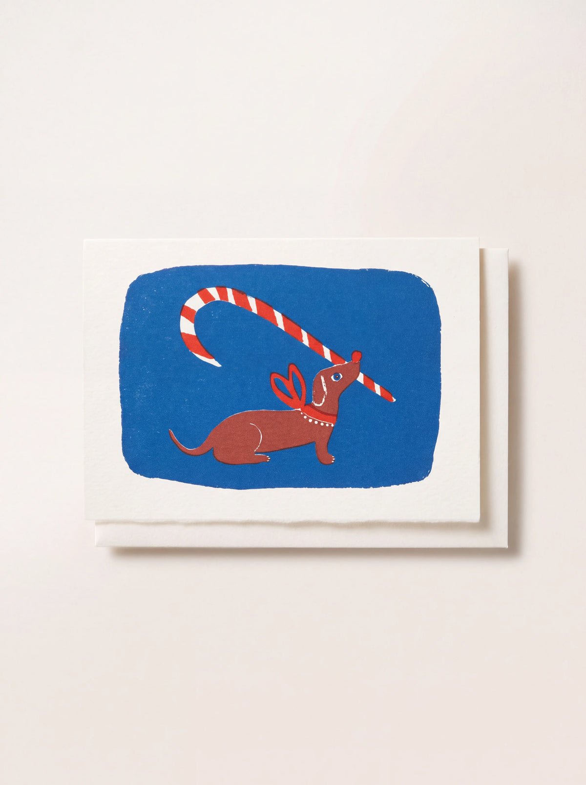 Paper greeting card illustrated with a brown dachshund holding a striped candy cane against a blue background
