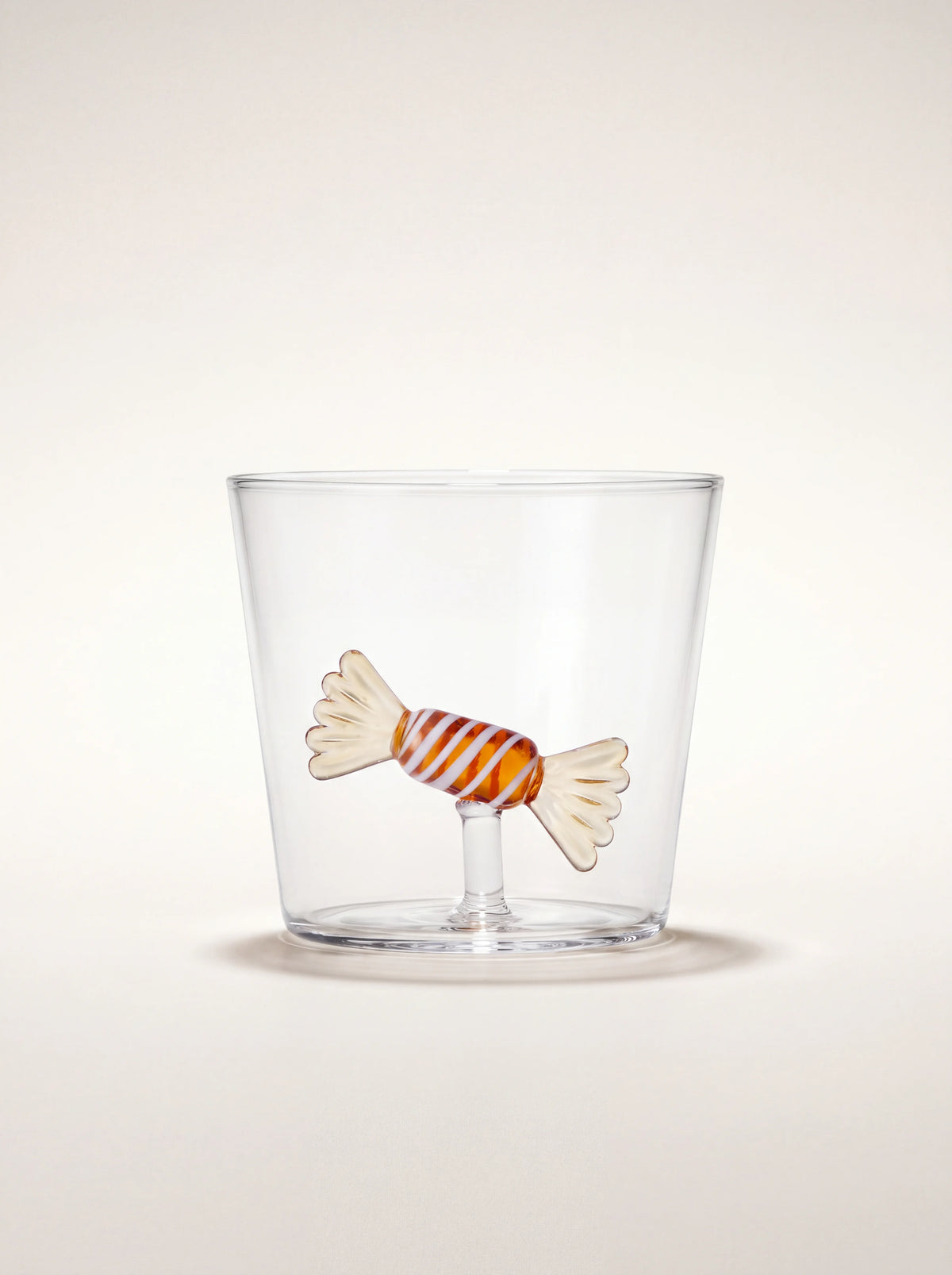 Clear borosilicate glass tumbler with an amber and white striped glass candy figure inside