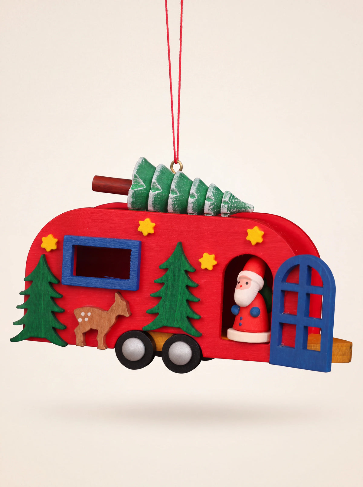 Red painted wooden caravan ornament with a rooftop tree, deer motif, and Santa figure inside the open door