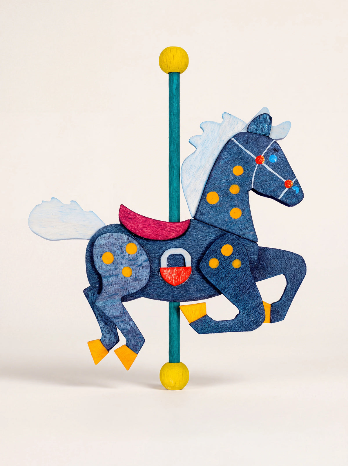 Dark blue wooden carousel horse ornament with yellow spots, a pink saddle, and a pole with yellow finials