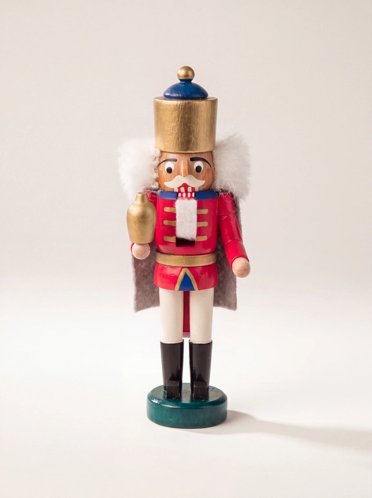 Painted wooden nutcracker in a red uniform and gold-coloured crown, holding a small golden vessel