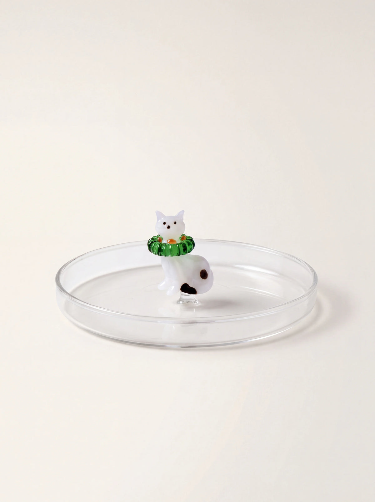 Clear borosilicate glass saucer with a raised rim and a centred white cat figurine wearing a green wreath