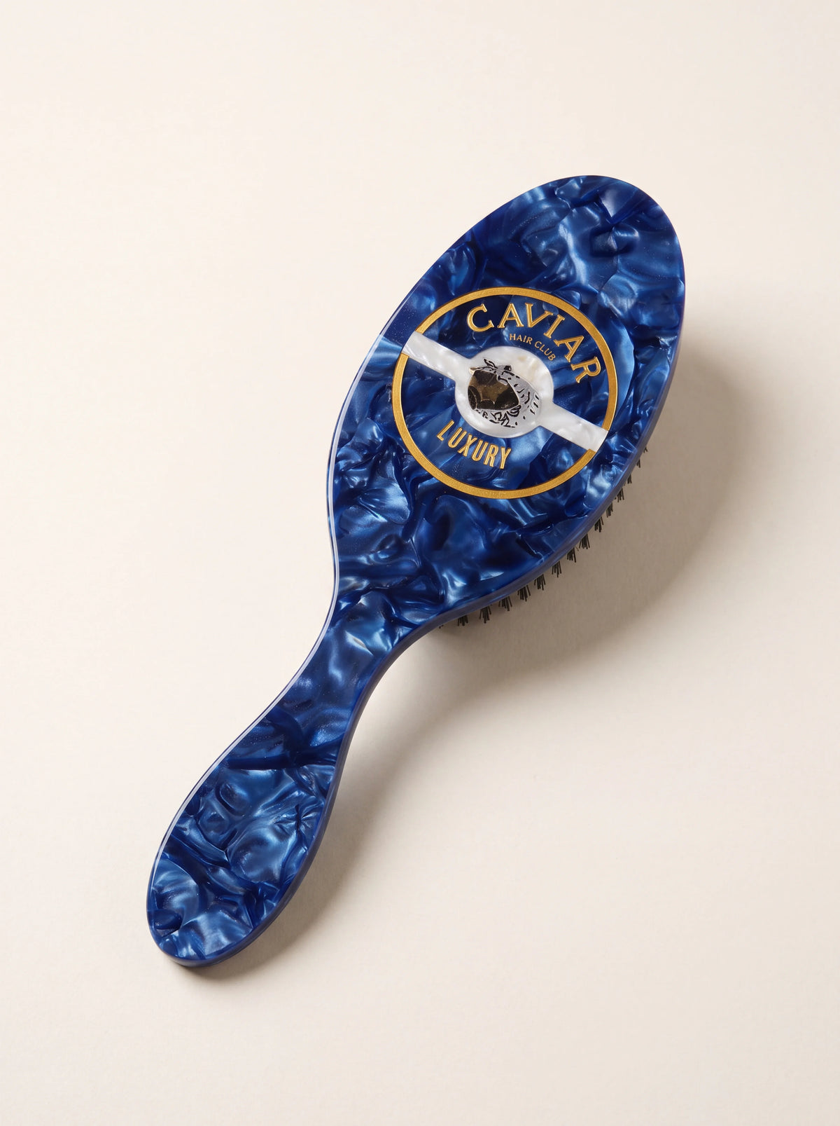 Oval cellulose acetate hairbrush in marbled blue with a Caviar Luxury motif on the reverse