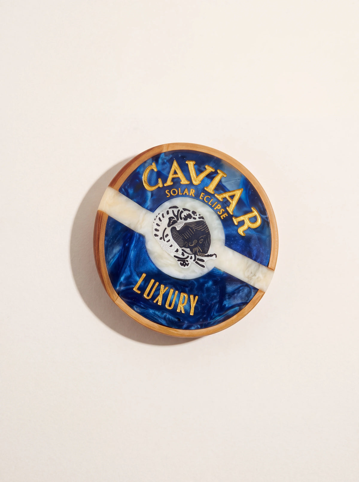 Acetate claw clip shaped like a round caviar tin in swirled blue and cream with gold lettering