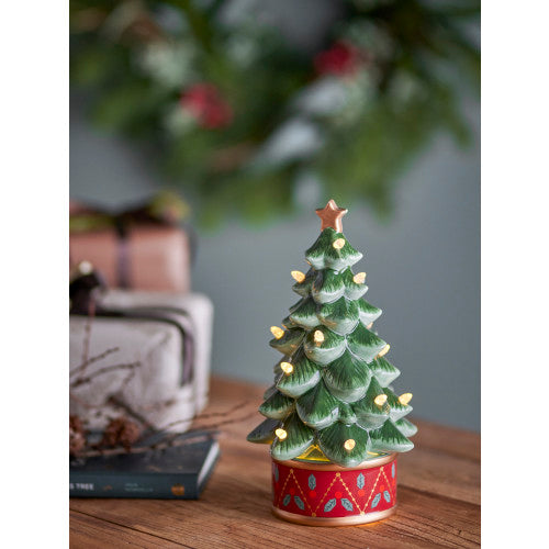 Green ceramic Christmas tree illuminated with warm lights on a wooden tabletop