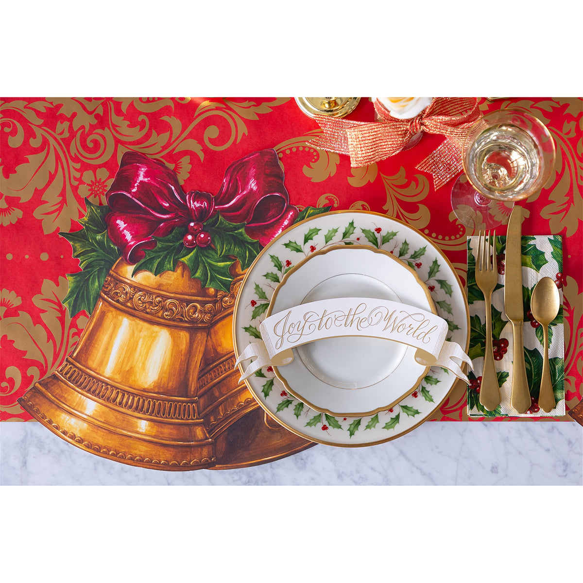 Christmas bell paper placemat laid under a plate with cutlery and a banner reading Joy to the World