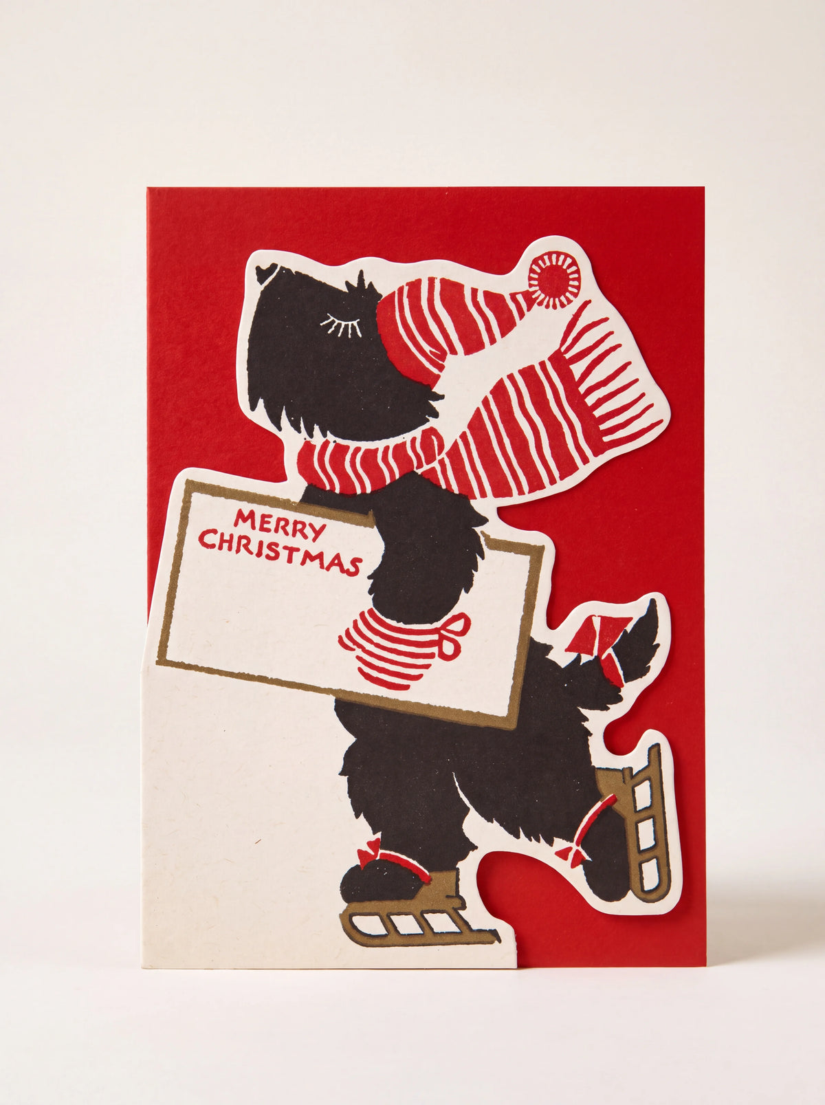 Cut-out Christmas card featuring an ice-skating black dog holding a sign reading MERRY CHRISTMAS