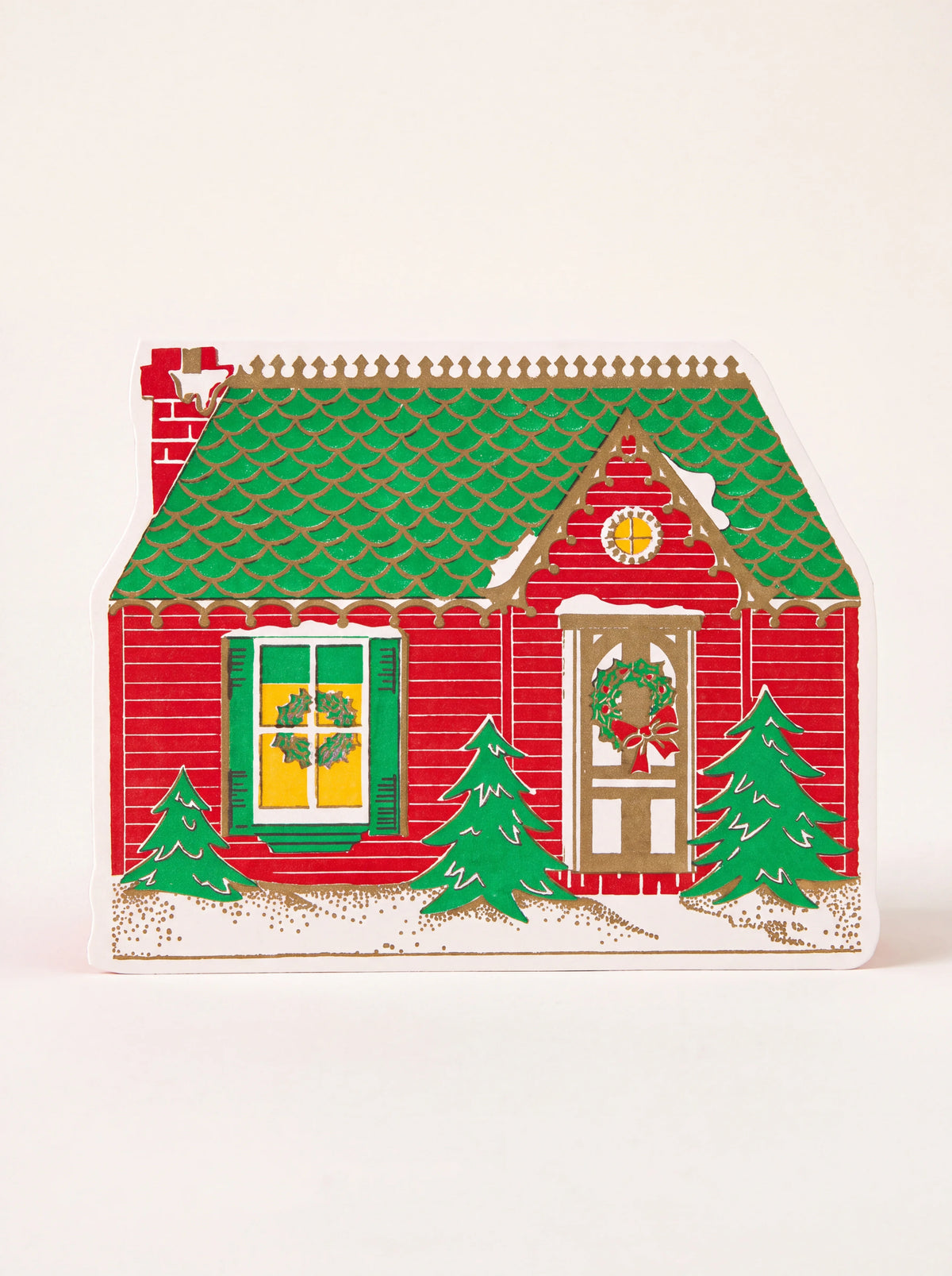 Cut-out paper Christmas card shaped like a red house with a green roof, gold details and fir trees
