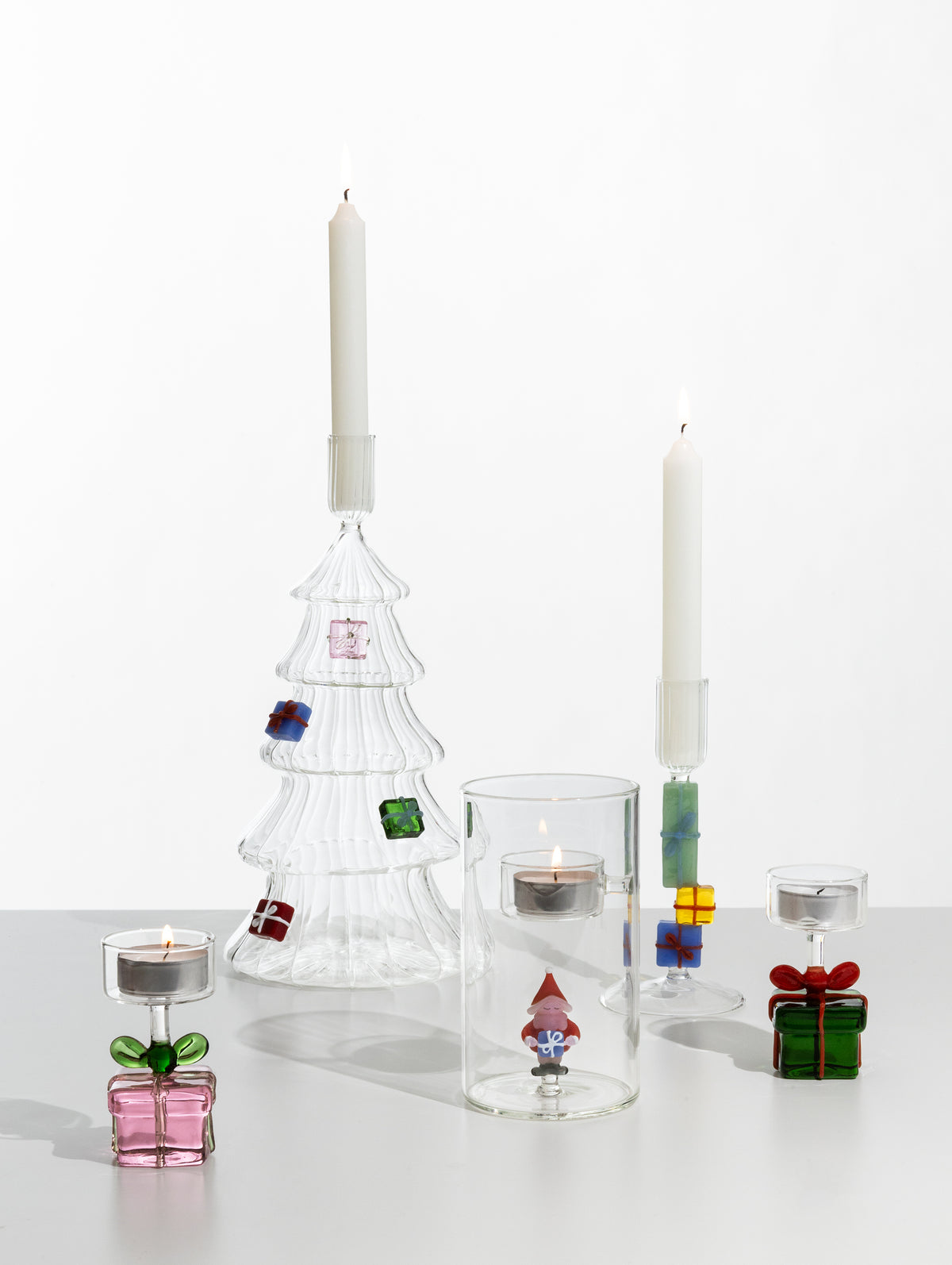 Glass Christmas tree candle holder holding a lit taper candle, shown arranged with other glass candle holders