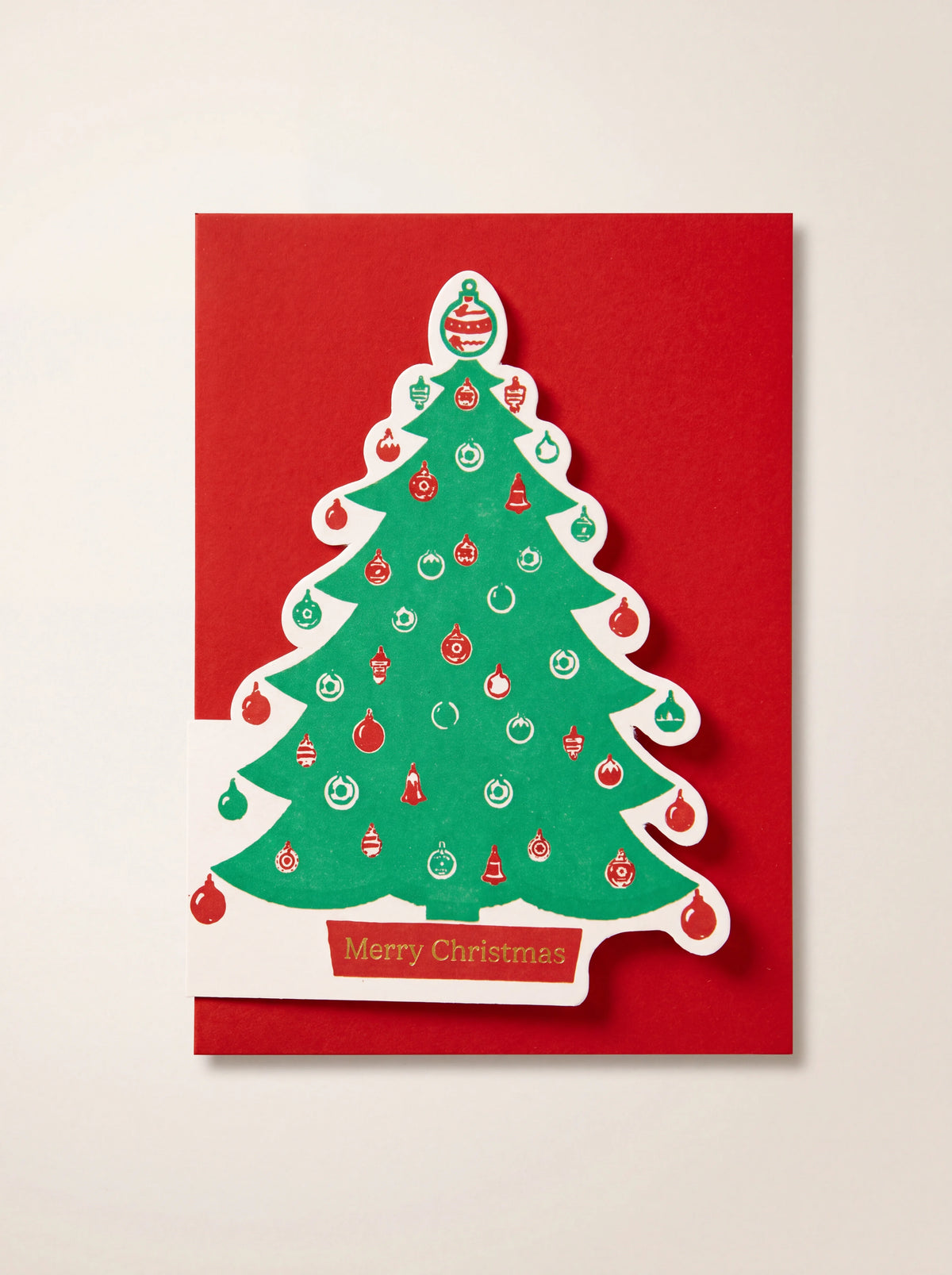 Red Christmas card featuring a die-cut green tree decorated with baubles and reading Merry Christmas