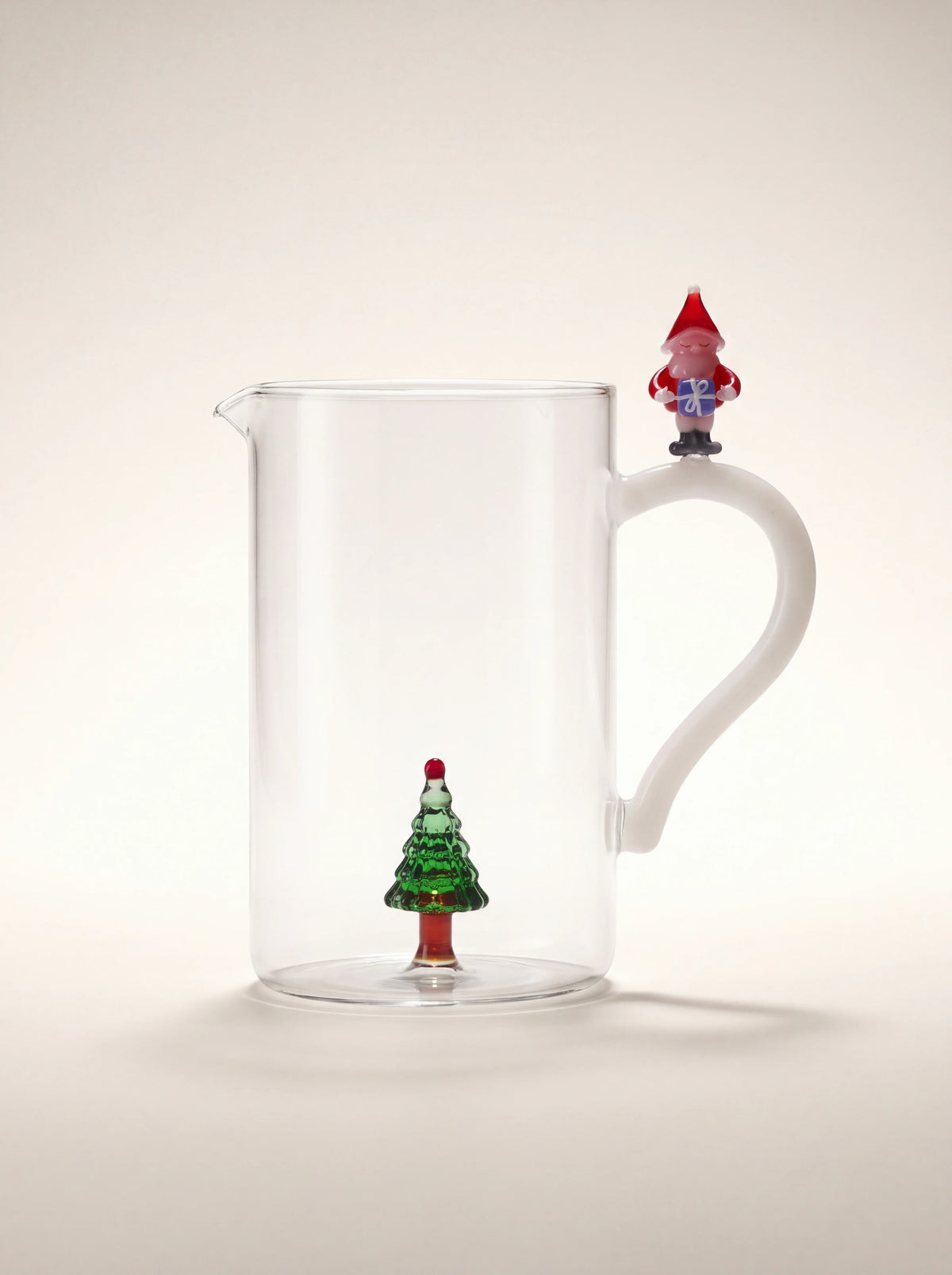 Clear glass jug with an internal green Christmas tree and a white handle topped with a Santa Claus figurine