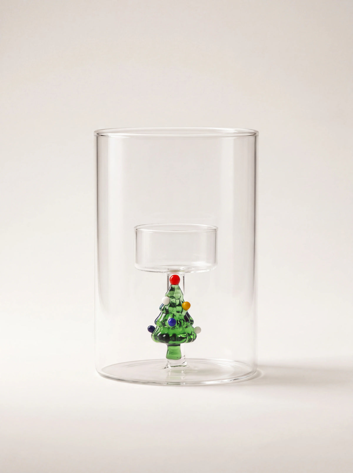 Clear cylindrical glass tealight holder with a raised inner cup resting on a small green Christmas tree