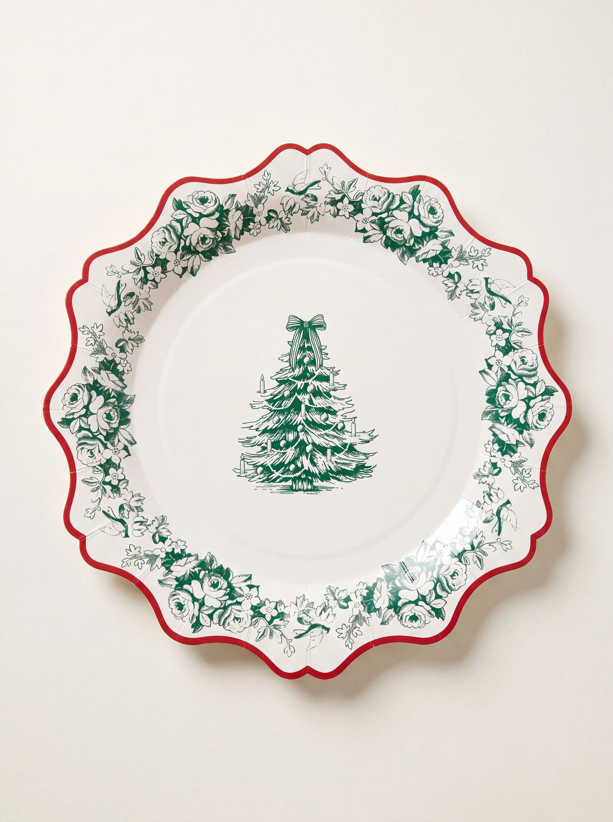 Round paper napkin with a red scalloped rim, green floral border and Christmas tree illustration
