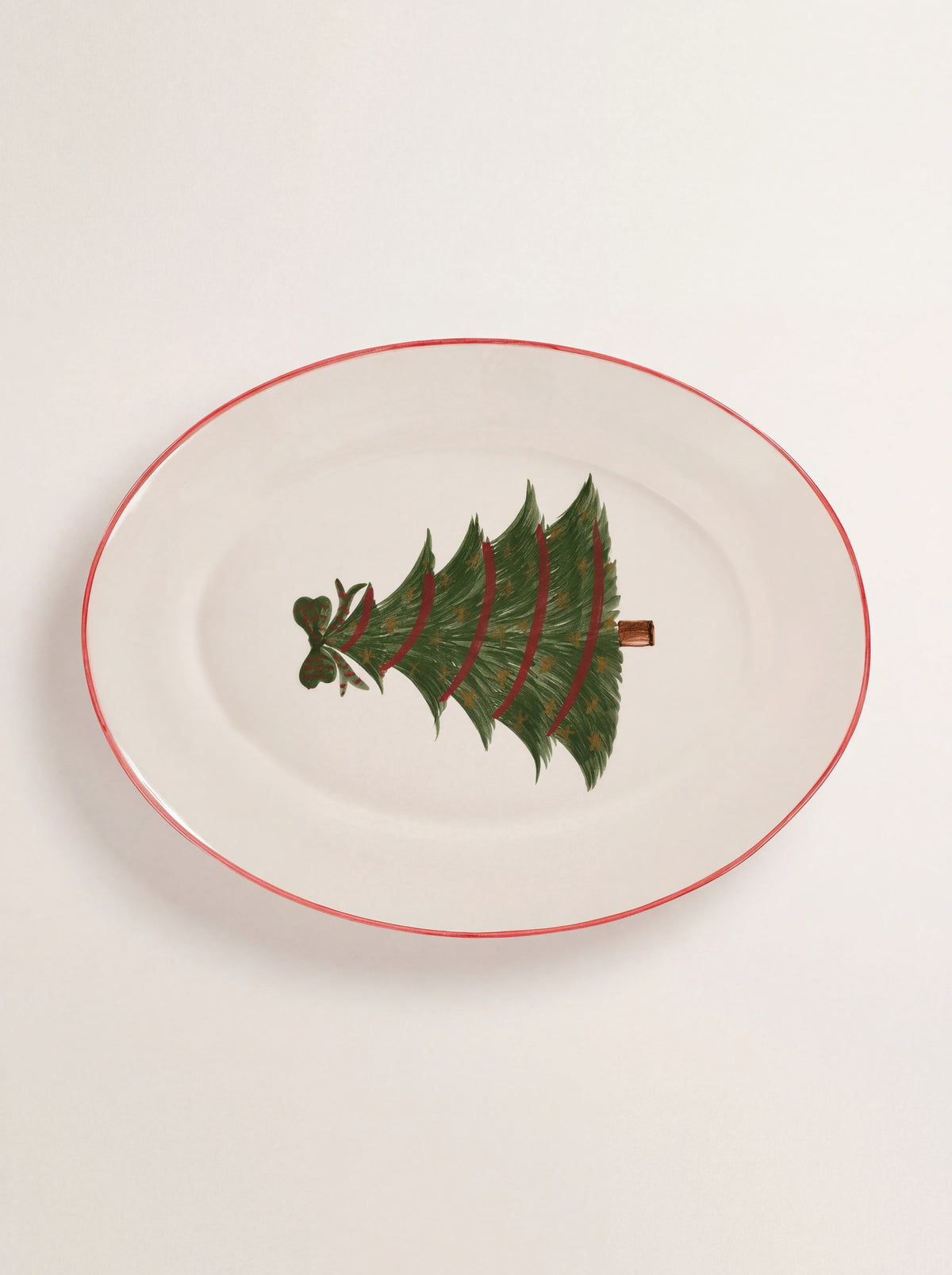 Oval earthenware serving platter in white with a red rim and a painted Christmas tree motif