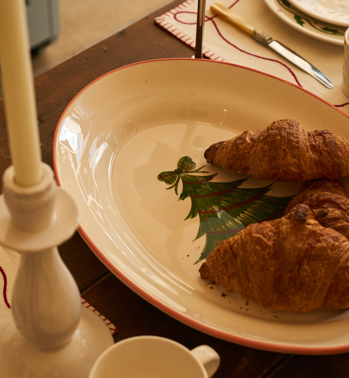 Oval earthenware serving platter holding croissants on a laid table beside a candlestick
