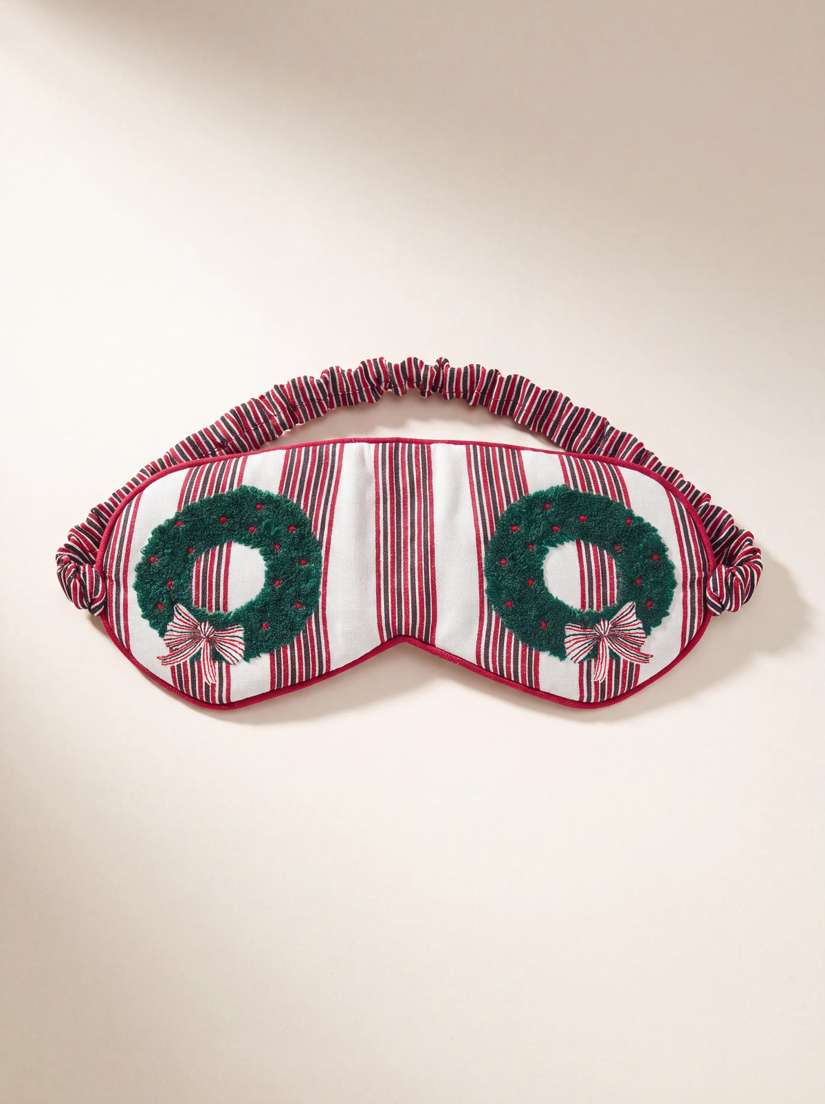 Red and white striped fabric sleep mask featuring two green wreath motifs with bows